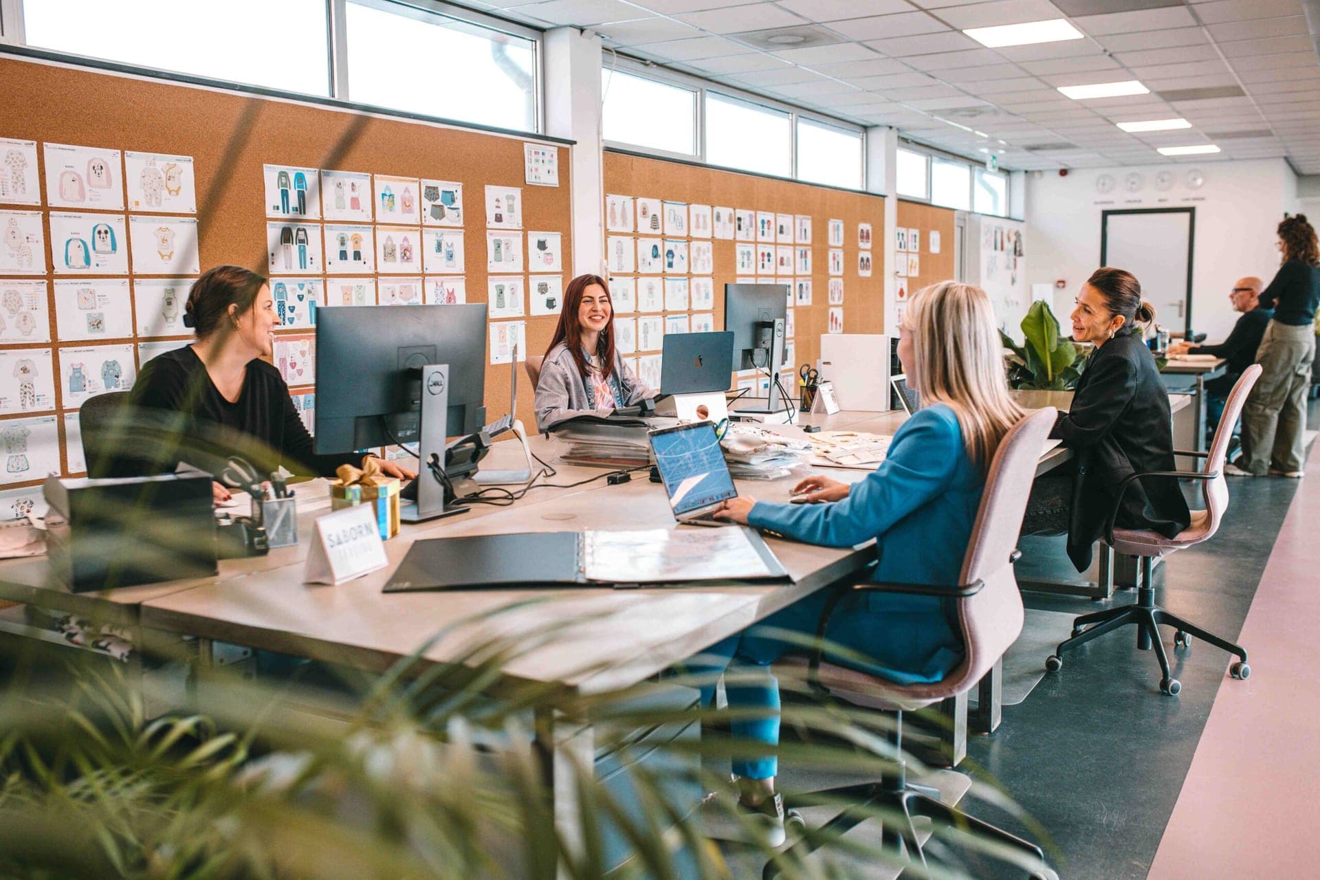 Het ontwerpteam werkt samen aan een gedeeld bureau, voor een kurkwand vol ontwerpbladen van kleding